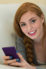 Fototapeta premium Happy redhead lying on the sofa sending a text