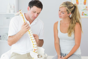 Handsome physiotherapist showing patient something on skeleton m