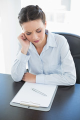 Frowning stylish brunette businesswoman looking at her clipboard