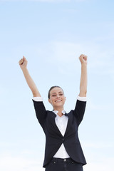 Young businesswoman with arms up against blue sky