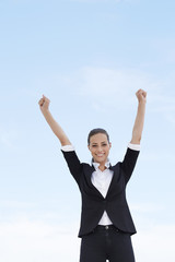 Young businesswoman with arms up against blue sky