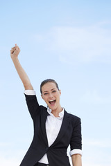 Young businesswoman punching air against blue sky