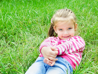 Cute smiling little girl lying in grass on the meadow