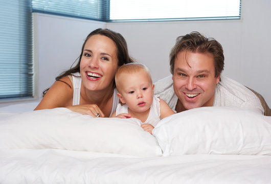 Happy loving family lying in bed with cute baby