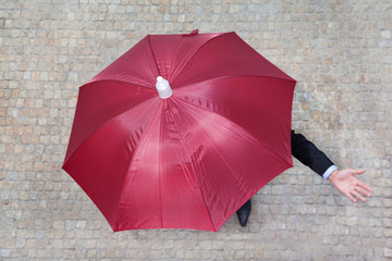 Businessman hidden under umbrella and checking if it's raining