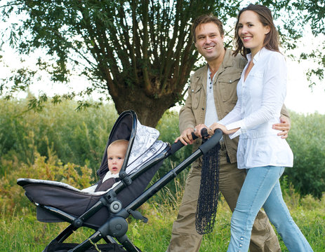 Father And Mother Smiling Outdoors And Walking Baby In Pram