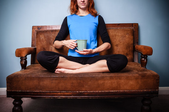 Young spiritual woman sitting on sofa drinking calming tea