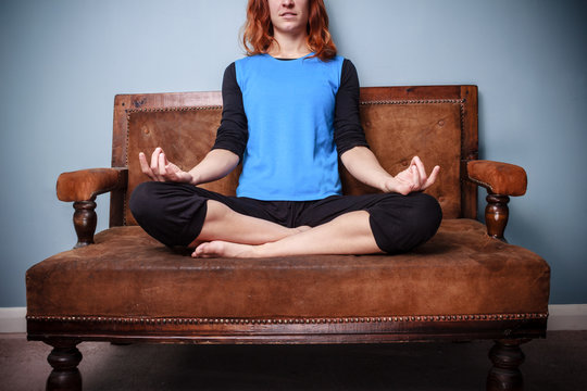 Spiritual young woman is meditating on an old sofa
