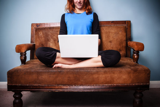 Calm young woman sitting on sofa with legs crossed using laptop