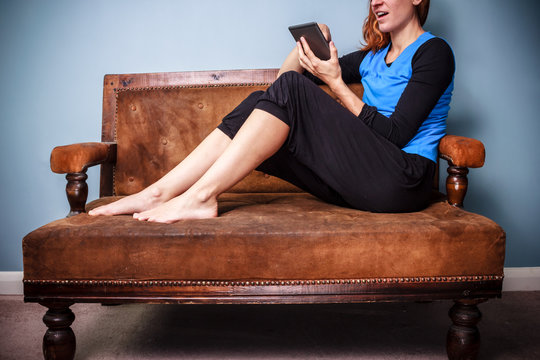 Young woman sitting on sofa reading digital book