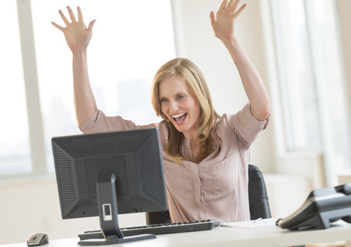 Successful Businesswoman With Arms Raised Looking At Computer