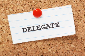 The word Delegate on paper note pinned to a cork notice board