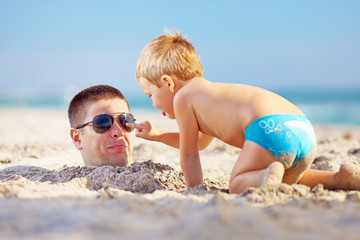 father and son having fun in sand on the beach