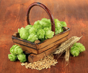 Fresh green hops in basket and barley, on wooden background