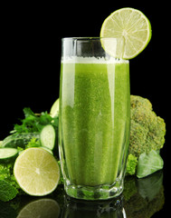 Glass of green vegetable juice and vegetables isolated on black