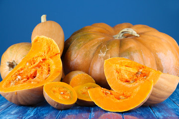 Ripe cut pumpkins on wooden table on blue background