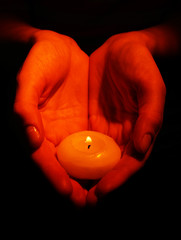 Burning candle in hands isolated on black