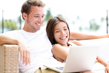 Couple in sofa with laptop pc at home laughing