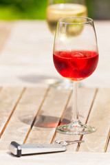 Glass of rose wine on wooden garden table with hotel key. Blurre
