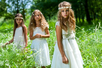 Three girls wearing white dresses in woods.