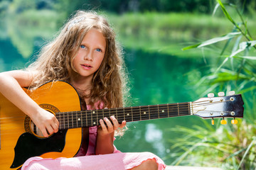 Young guitar student playing at lake.