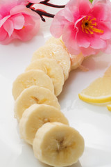 Sliced banana on white plate decorated with sakura and lemon