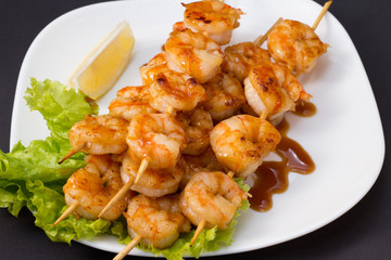 Shrimp shashlik on white plate with sauce and salad