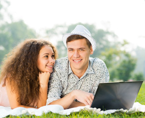 couple lying together in a park with laptop