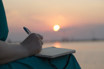 Naklejka premium Woman writing in her diary at sunset