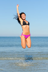 Happy woman jumping in the water at the beach