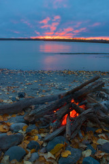 Lit campfire on the shore of Talkeetna river with red sunset