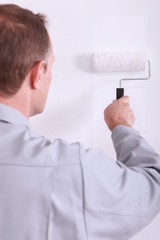 Man painting a wall white with a roller