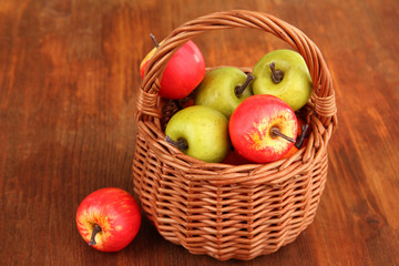 Small apples in wicker basket on wooden background