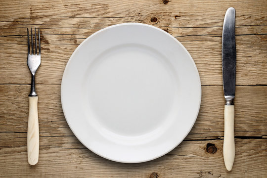 Empty plate, old fork and knife on wooden background