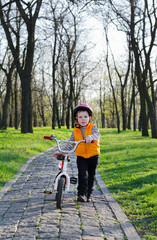Little boy pushing his bicycle in a park