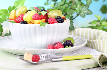 Fruit salad in bowl, on wooden table, on bright background