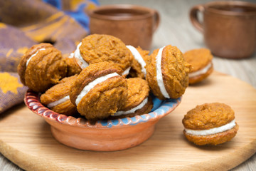 bowl of pumpkin cookies with cream filling on a wooden board