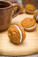 Pumpkin cookies with cream filling and cup of tea on board