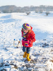 Fototapeta na wymiar Small girl pulling a sledge in a snow covered dune landscape