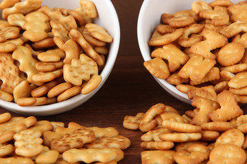 Delicious crackers in bowls on wooden table on brown background