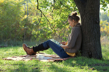 Hipster girl leaning on a tree and using tablet computer