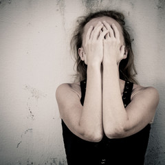 one sad woman sitting on the floor near a wall and holding her h