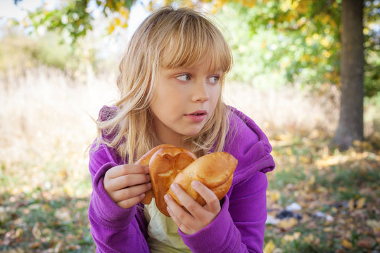 Little blond girl in autumn park holds small pies