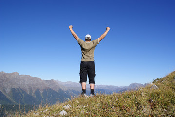 A man stands on a hillside with their hands up