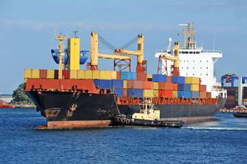 Tugboat assisting container cargo ship to harbor quayside