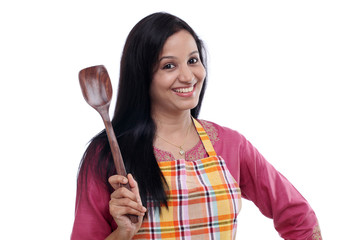Young Indian woman holding kitchen utensil against white