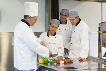 Smiling head chef teaching how to slice vegetables - Powered by Adobe