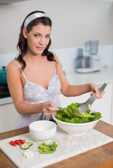 Obraz na płótnie Canvas Smiling cute brunette mixing healthy salad