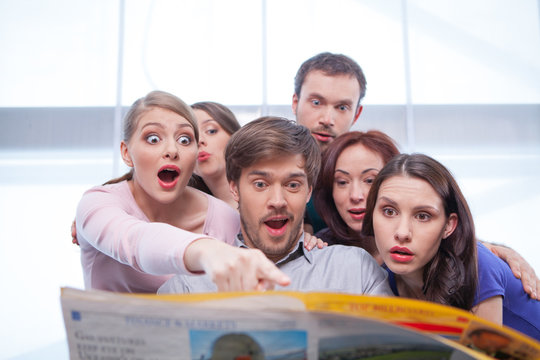 Group of young people reading newspaper.