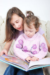 Fototapeta premium Sisters sitting in living room reading book